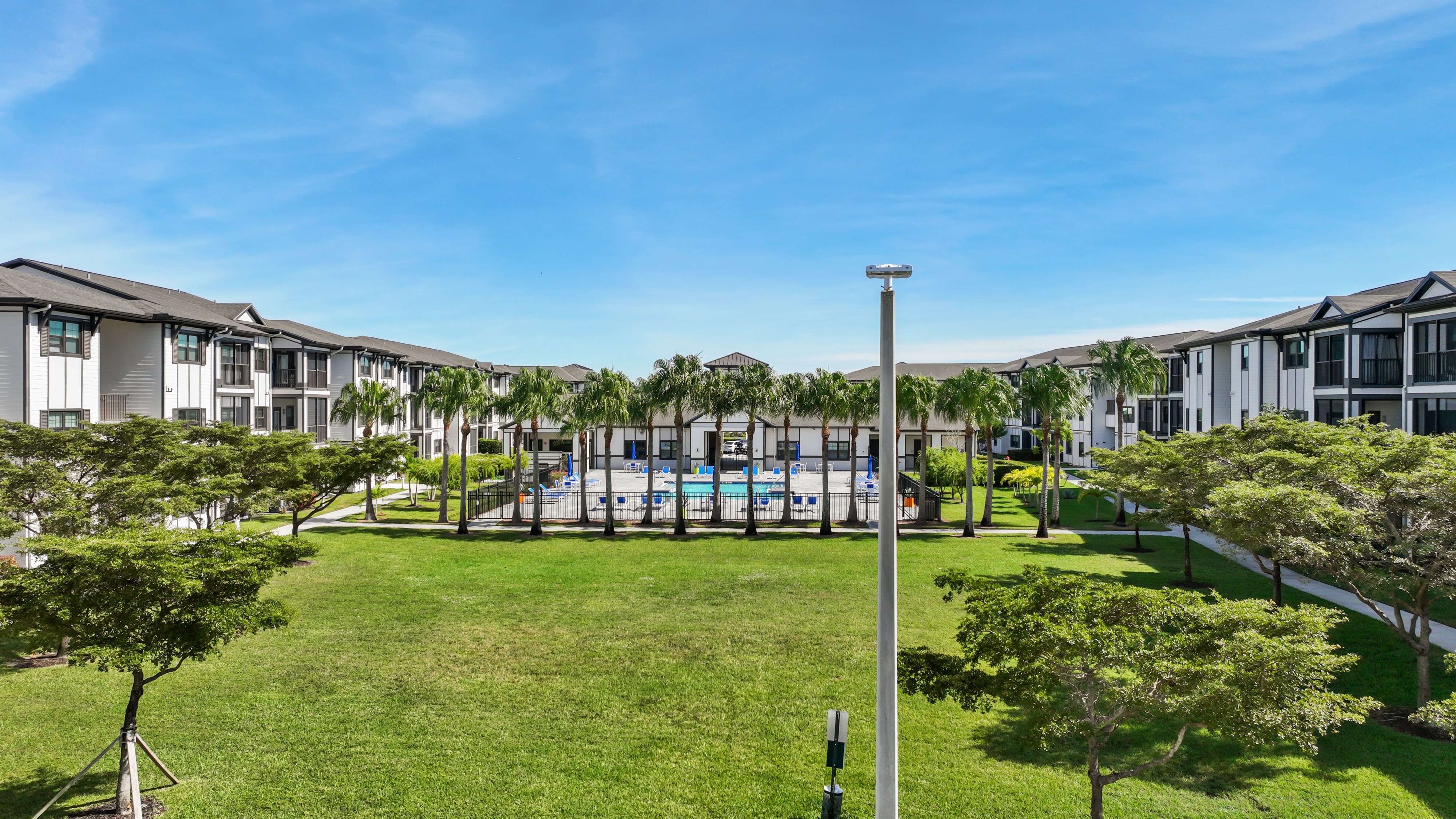 A sunny day at a residential complex with a grassy area and a pool.